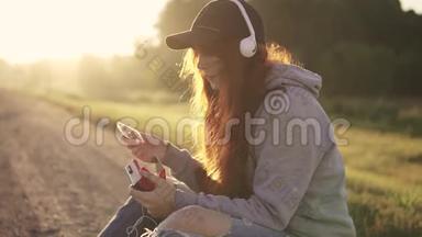 女孩希普斯特插入一个盒式磁带播放器，并听音乐耳机在日落。 一幅肖像画